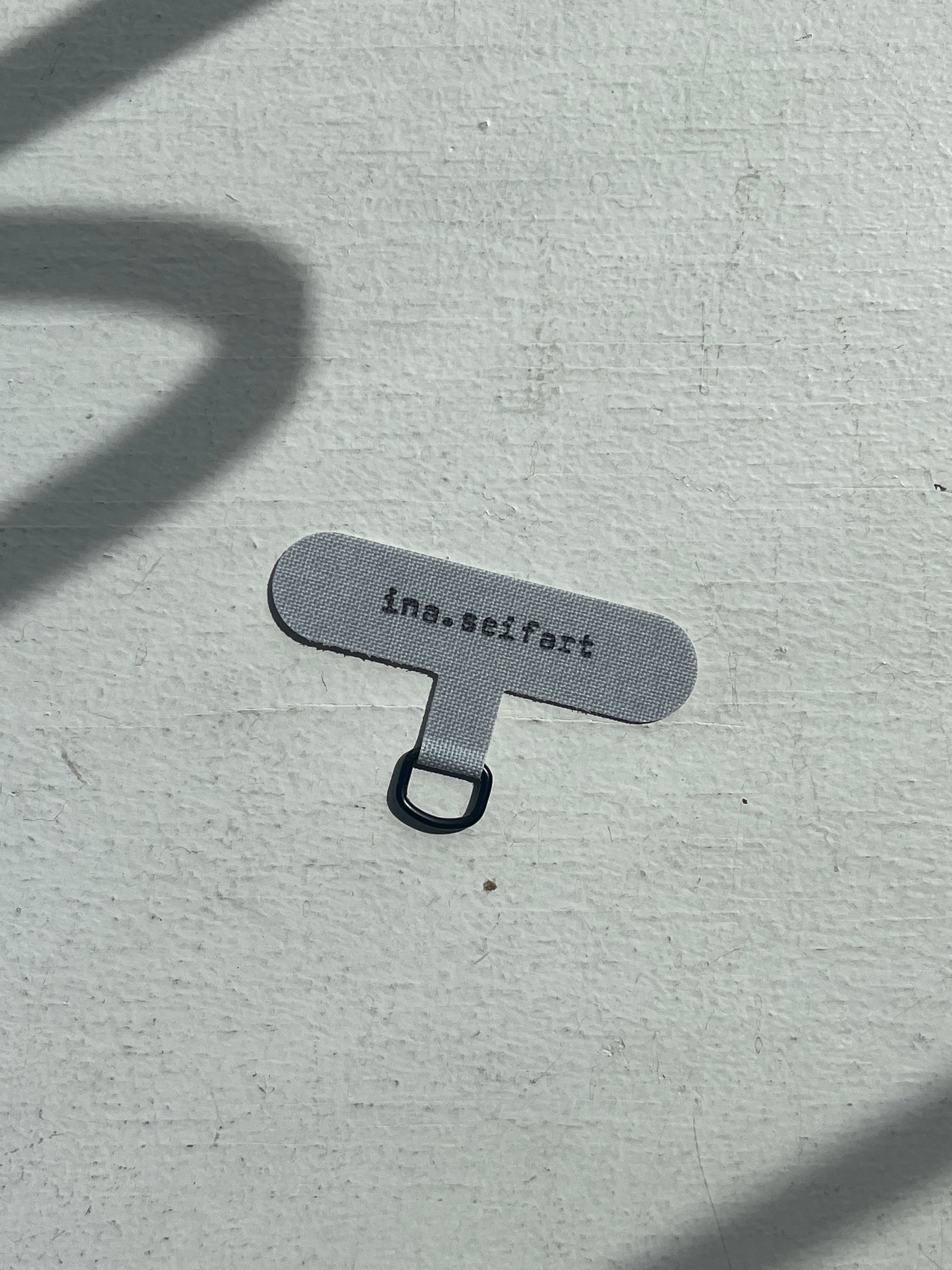 Ina Seifart - Phone Case Adapter - a grey insert that goes  between your phone and phone case, with a little black loop for attaching the phone necklace to