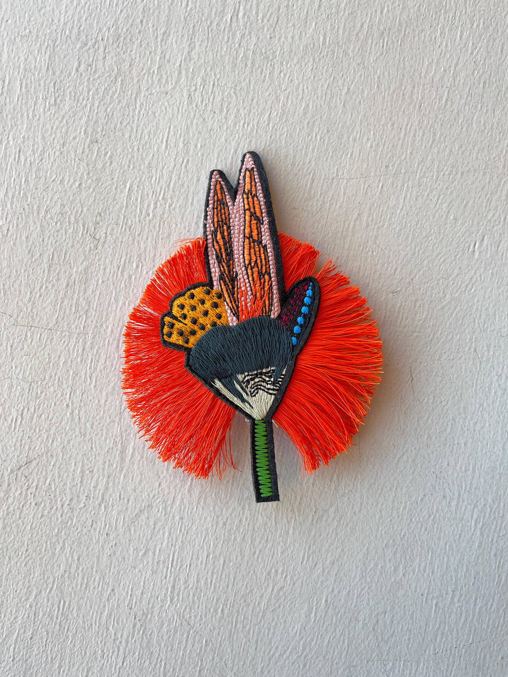 Decorative brooch with orange feather-like design and butterfly pattern on a light gray background