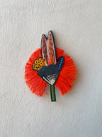 Decorative brooch with orange feather-like design and butterfly pattern on a light gray background
