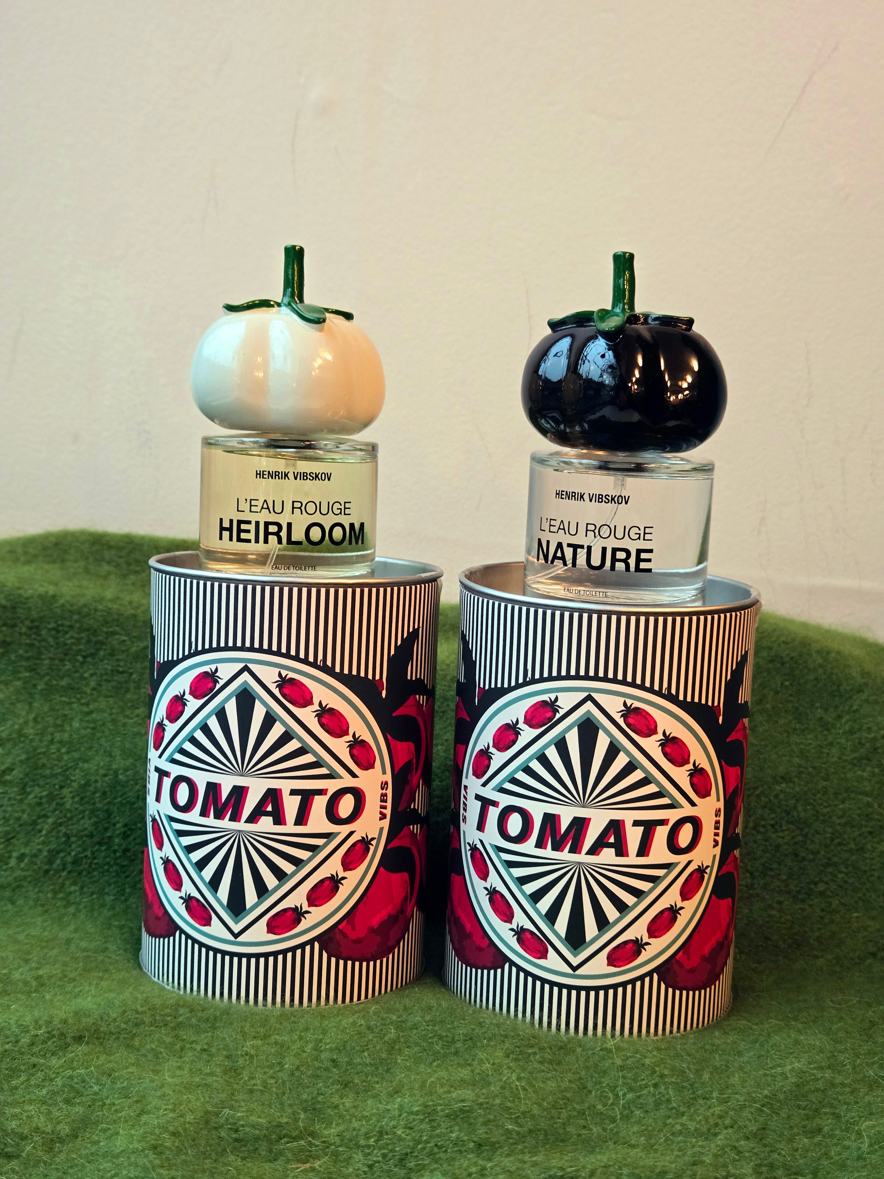 Two bottles of Heurloom Tomato L'Eau Rouge with decorative labels on a green surface.