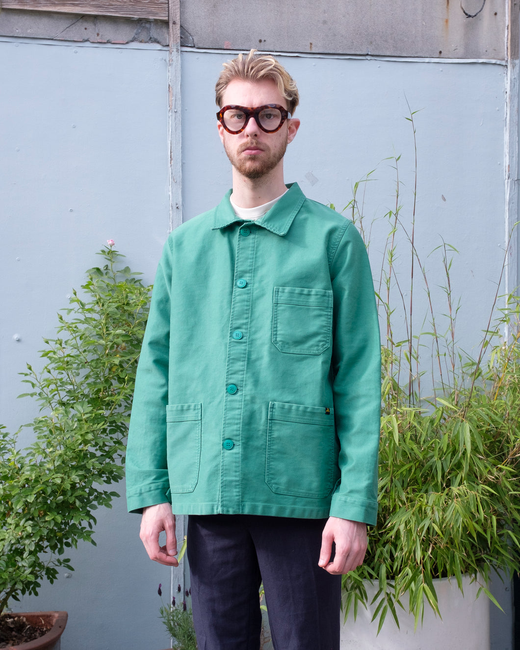 Le mont st michel - Genuine Work Jacket (Men's) - Green Twill - front. This image depicts the model wearing the genuine work jacket in a refreshing cold tone vibrant green with color matched buttons. it has 3 pockets, one located at the left chest and two at the waist. 