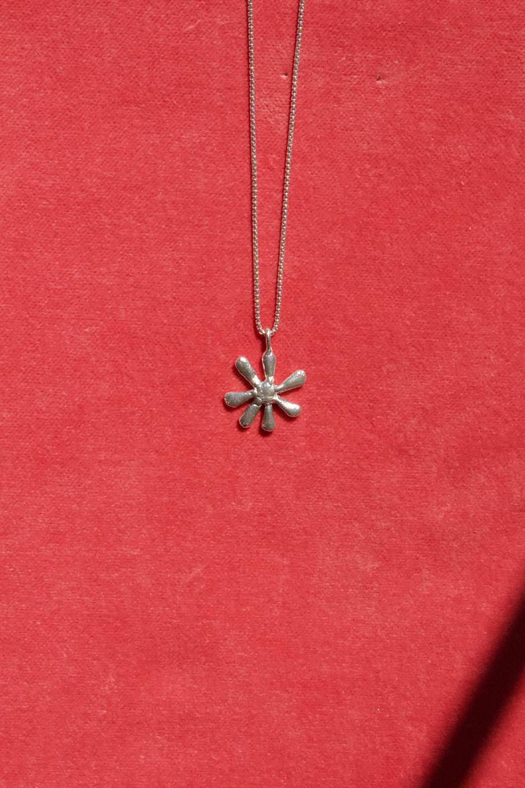 Daisy pendant necklace from Erica Leal. This necklace has a delicate thin chain, and a abstract 7-petal daisy pendant charm as the focal point. all parts of this necklace are sterling silver, and is handmade from start to finish in Vancouver, BC. 