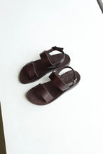 Load image into Gallery viewer, A brown leather strap sandal with buckle ankle strap. They feature visible topstitching around the leather sole as well as a leather logo embossed detail on the heel of the sole 
