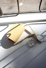 Load image into Gallery viewer, A butter yellow demi lune mini bag sitting on a window box, this rich leather bag has a soft yellow colour tone 

