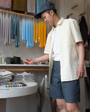 Load image into Gallery viewer, Mac looking very coordinated in OFS&#39;s new short and matching 6 panel cap in formal ticking, styled with Minimum&#39;s Natheo Shirt in white asparagus. - side/looking at candles
