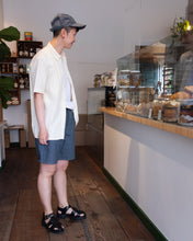 Load image into Gallery viewer, Mac looking very invested in pastries wearing OFS&#39;s new short and matching 6 panel cap in formal ticking, styled with Minimum&#39;s Natheo Shirt in white asparagus. - side/happy mac
