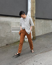 Load image into Gallery viewer, Old Fashion Standards&#39; Workhorse Trouser back in Tobacco! The image depicts Mac walking down the alleyway in the trousers and its matching 6 panel cap, completing her look with Minimum&#39;s Thao Shirt in grey pinstripe. The workhorse trousers give Mac lots of storage space totalling at 6 pockets with the extra pair at thigh height in addition to classic front and back pockets. Staff at Eugene Choo recommends these pants for everyone, but especially those plagued with pokey pocket wallets or phones! 
